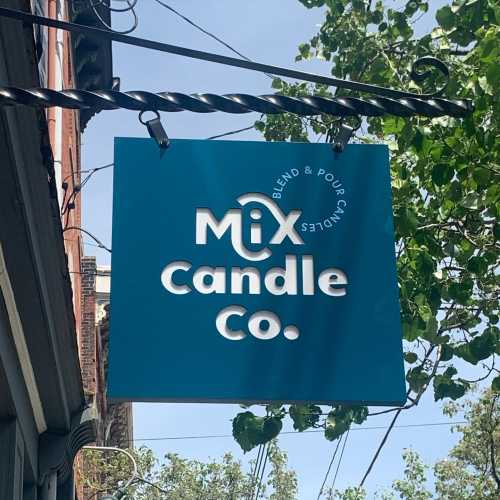 Sign for "Mix Candle Co." featuring a blue background with white text, hanging from a decorative bracket.