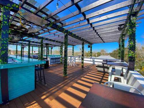 A rooftop terrace with wooden flooring, green vines on beams, and seating areas under a clear blue sky.