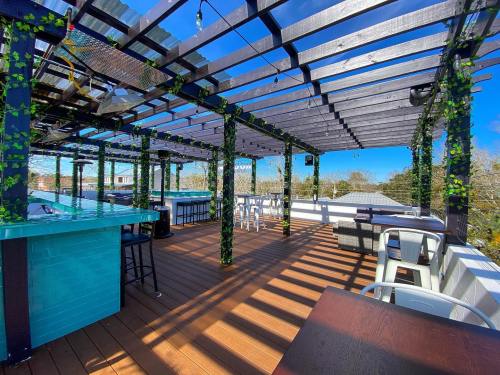 A rooftop terrace with wooden flooring, green vines on beams, and seating areas under a clear blue sky.