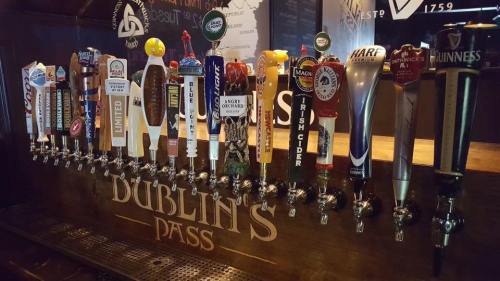 A row of various beer taps labeled with different brands at a bar, featuring a sign that reads "Dublin's Pass."