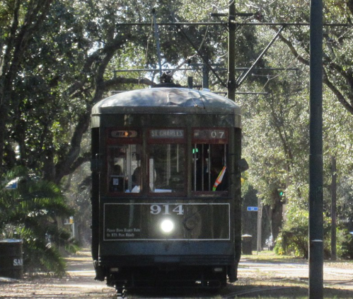 A vintage green streetcar labeled "914" travels along a tree-lined track on a sunny day.