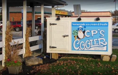 Sign for CP's Cooler, featuring a penguin logo, advertising homemade ice cream and treats outside a small building.