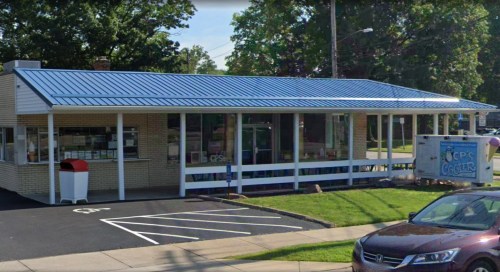 A one-story building with a blue metal roof, large windows, and a sign for ice cream, surrounded by parking spaces.