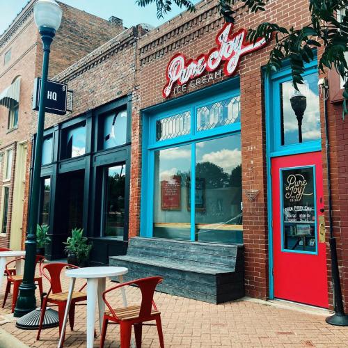 A charming ice cream shop with a red door, large windows, and outdoor seating on a quaint street.