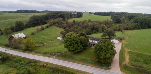 Aerial view of a rural landscape featuring a house, trees, and fields, with a road running alongside.