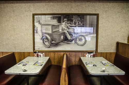 A vintage photo of a delivery vehicle hangs on the wall of a diner with empty booths and tables.