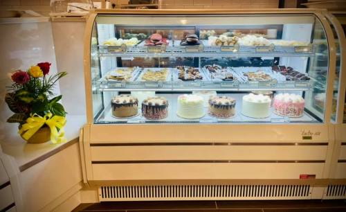 A display case filled with various cakes and pastries, alongside a bouquet of roses in a vase.
