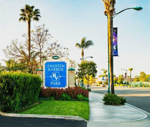 Sign for Anaheim Harbor Park, surrounded by palm trees and greenery, with a clear blue sky in the background.