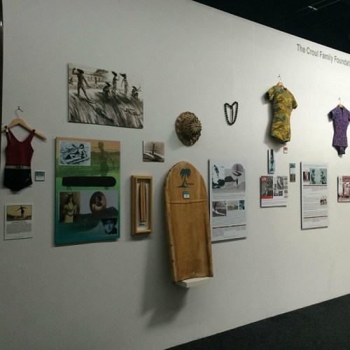 Art exhibition wall featuring various artworks, including clothing pieces and informational panels.