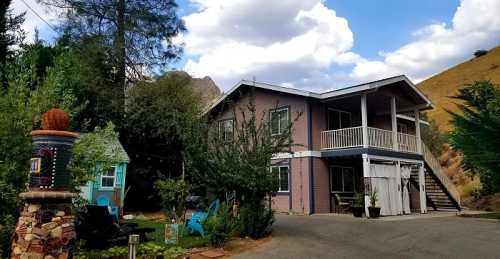 A two-story house surrounded by trees and hills, with a porch and colorful outdoor furniture.