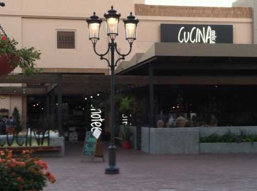 Exterior view of a restaurant named "Cucina," featuring outdoor seating and decorative street lamps.