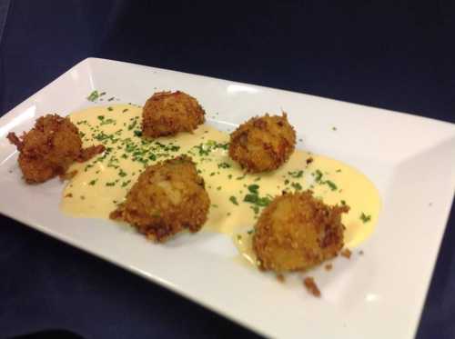 Five golden-brown fried balls on a white plate, drizzled with creamy sauce and garnished with green herbs.