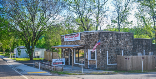A stone building with a sign reading "Heidi's" and an American flag, surrounded by trees and a quiet street.