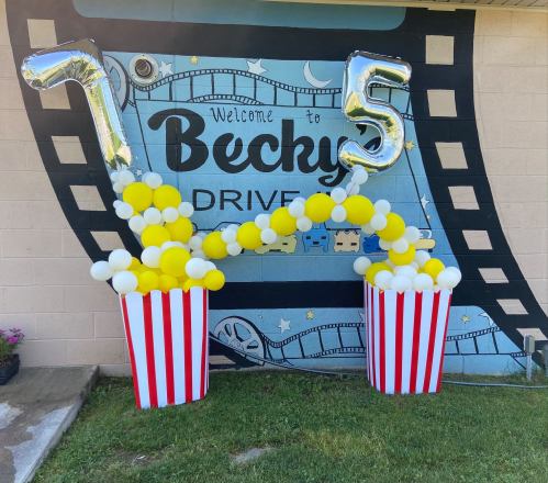 A festive display with large silver balloons reading "75" and yellow and white balloons in striped popcorn boxes.