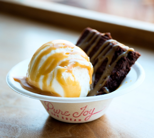 A bowl of vanilla ice cream topped with caramel sauce, alongside a chocolate brownie.