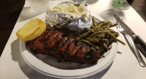 A plate with grilled steak, green beans, a baked potato wrapped in foil, and a slice of bread.