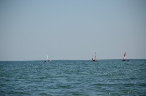 Three sailboats with white and red sails on a calm blue sea under a clear sky.