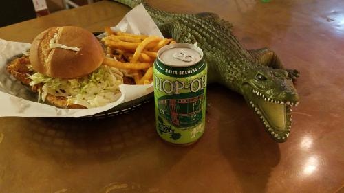 A plate with a sandwich, fries, and a can of beer next to a toy alligator on a wooden table.