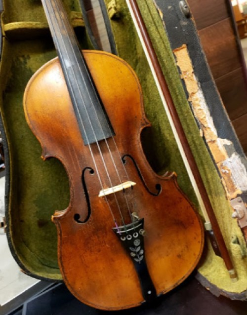 A vintage violin resting in a worn green velvet case, with a bow beside it.