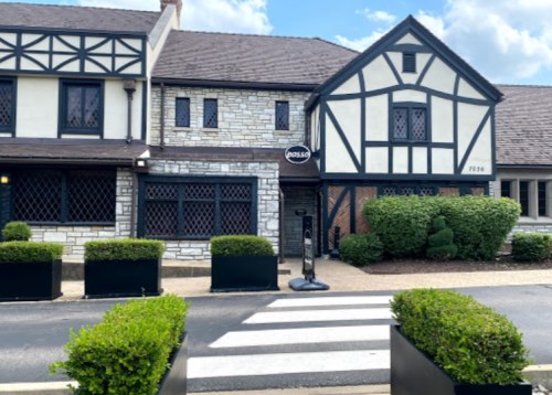A Tudor-style building with stone and wood accents, featuring a sign and landscaped greenery in front.