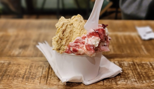 A cup of ice cream with two flavors: a light brown scoop and a pink, swirled scoop, resting on a wooden table.