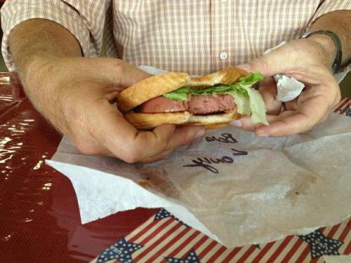 A person holds a sandwich with lettuce and a meat patty, resting on a table with a patriotic tablecloth.