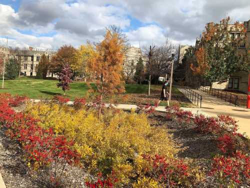 A vibrant park scene with colorful autumn foliage, featuring red and yellow plants under a partly cloudy sky.