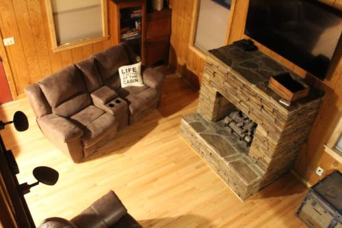 Cozy cabin living room with a stone fireplace, a brown couch, and a sign that reads "LIFE AT THE CABIN."