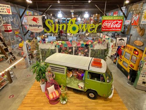 A vibrant vintage shop interior featuring a green VW van, retro signs, and eclectic decor in a lively atmosphere.