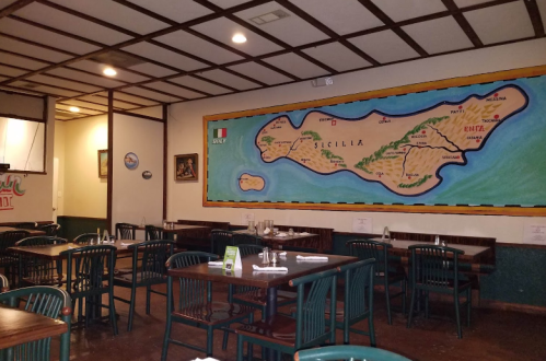 Interior of a restaurant featuring wooden tables, green chairs, and a large map of Sicily on the wall.