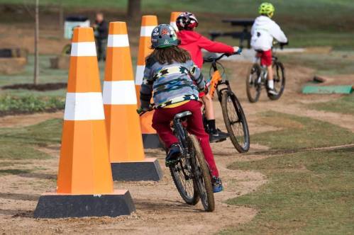 Three children riding bikes on a dirt track, navigating around orange traffic cones.