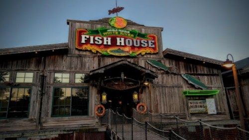 Exterior of the White River Fish House, featuring a rustic wooden facade and a colorful sign, with a hiring notice visible.