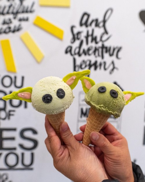 Two ice cream cones shaped like a character with green ears and eyes, held against a colorful, motivational background.