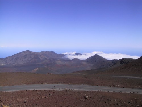 A panoramic view of mountains with a clear blue sky and clouds hovering over the valley below.
