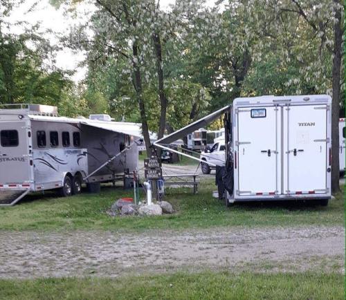 Two horse trailers parked at a campsite, with awnings extended and trees in the background.