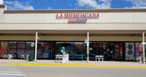 Exterior of La Michoacana store with colorful signage and outdoor seating under a blue sky.