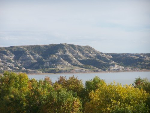 Scenic view of a lake with colorful trees in the foreground and a rugged hillside in the background under a cloudy sky.