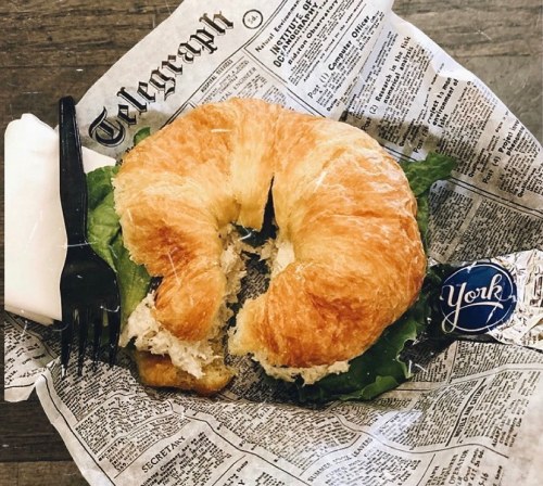 A croissant sandwich with lettuce and filling, served on newspaper print with a fork and a York sticker.