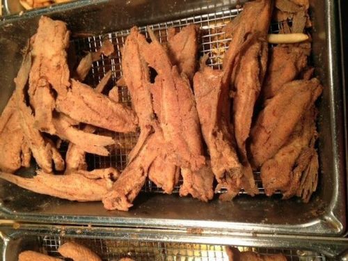 Fried fish fillets arranged in a metal tray, showcasing a crispy golden-brown texture.