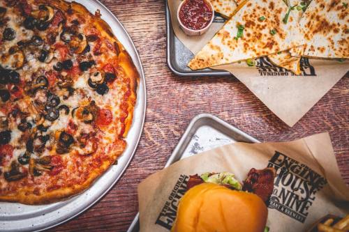 A table with a pizza topped with mushrooms and olives, quesadillas, and a burger on a tray.