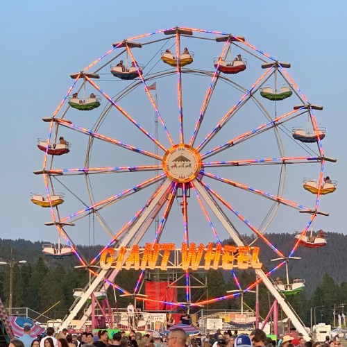 A colorful Ferris wheel lit up at dusk, with people enjoying a fairground atmosphere below.