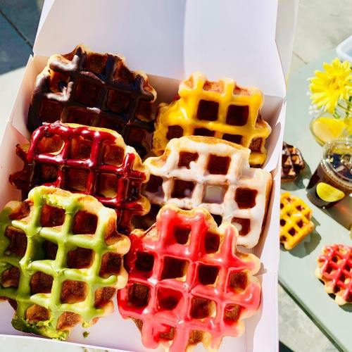 A box of colorful waffles in various flavors, including red, yellow, green, and brown, with syrup on the side.