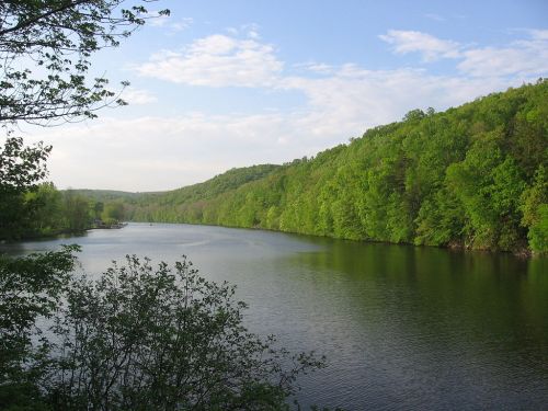 A serene river flows through lush green hills under a partly cloudy sky.