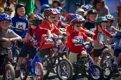 A group of young children in helmets and colorful shirts, ready to race on their bicycles at an event.