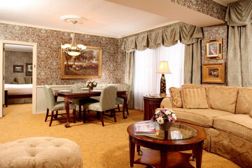 Luxurious hotel suite featuring a cozy living area, dining table, and elegant decor with floral accents.