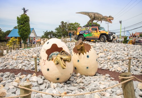 Dinosaur-themed attraction featuring hatching dinosaur eggs and a dinosaur statue on a vehicle in a rocky landscape.