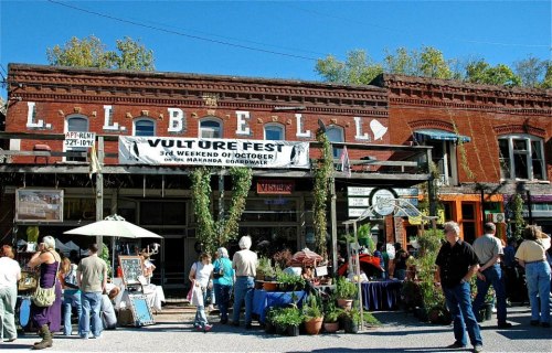 A bustling street scene featuring a historic building with a "Vulture Fest" banner and people browsing outdoor stalls.