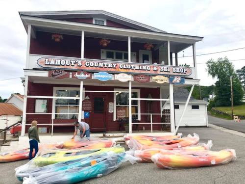 A red building with a sign reading "Lahout's Country Clothing & Ski Shop," featuring colorful kayaks in front.