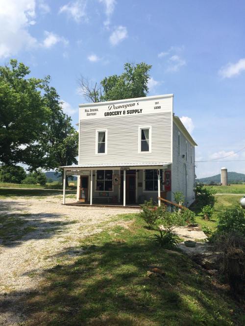 Historic grocery store with white siding, "Dunagan's Grocery & Supply" sign, surrounded by greenery and blue sky.