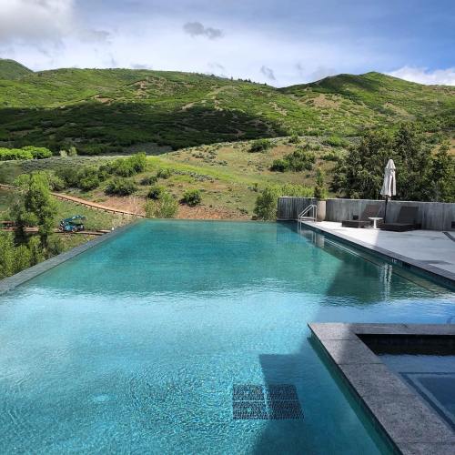 A serene infinity pool overlooking lush green hills under a clear sky.